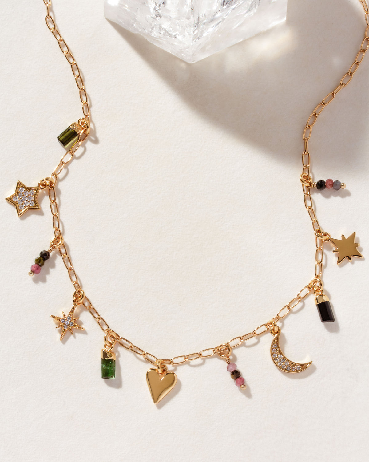 A gold-tone charm necklace with a variety of charms including stars, hearts, and moon shapes, as well as different colored beads.