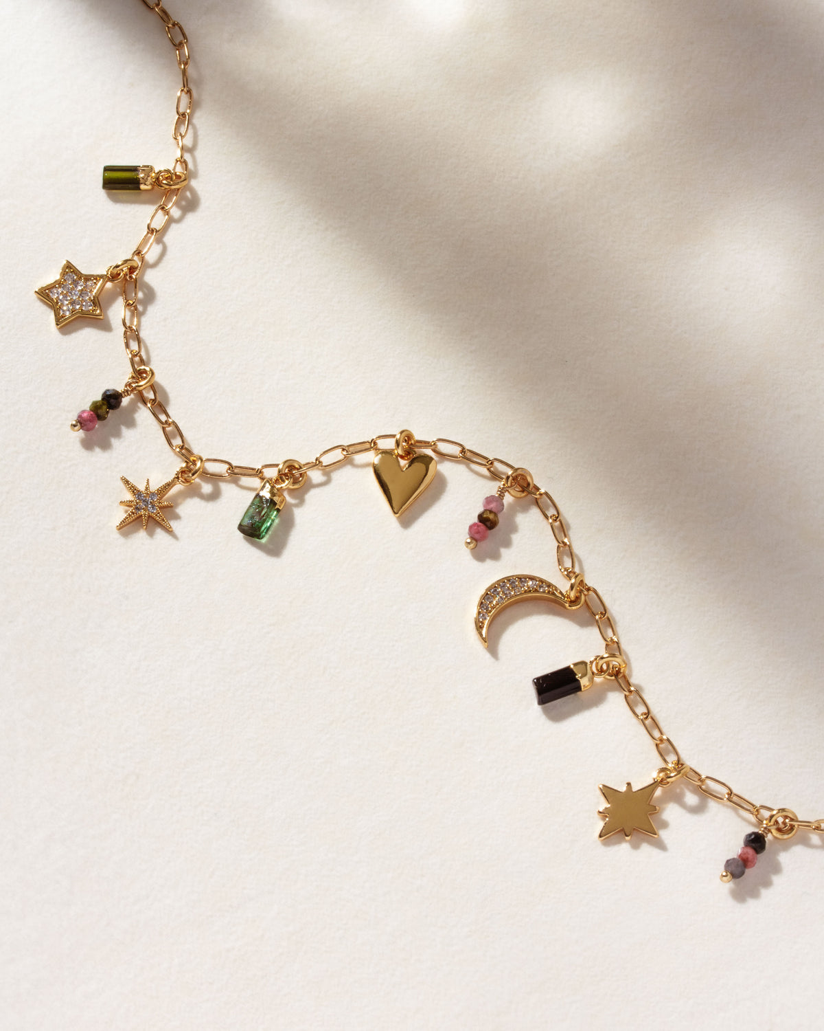 A gold-tone charm necklace featuring various celestial and heart-shaped charms, with labradorite, onyx, and coffee moonstone gemstones.