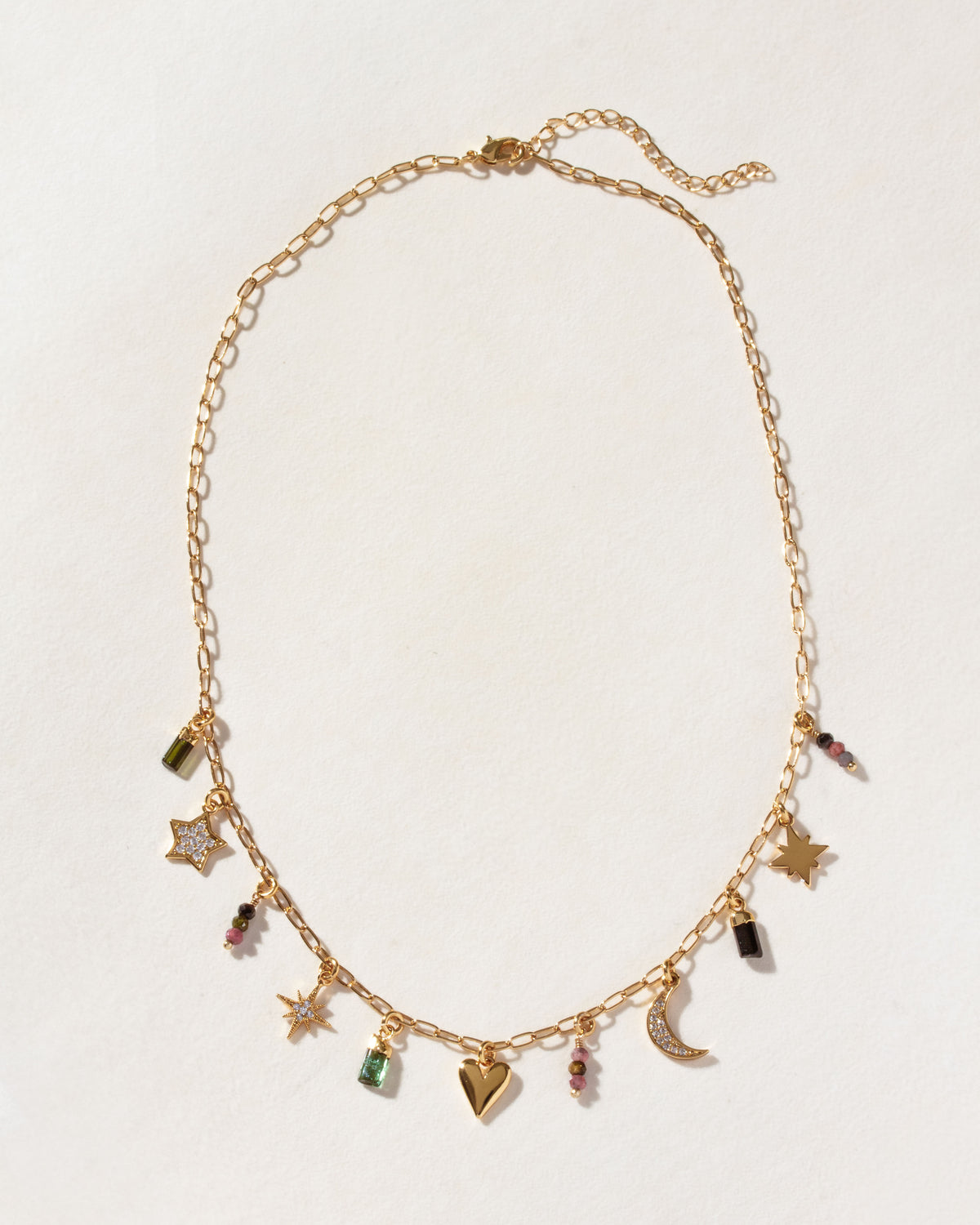 A gold-tone charm necklace featuring various celestial and heart-shaped charms, with various gemstones.