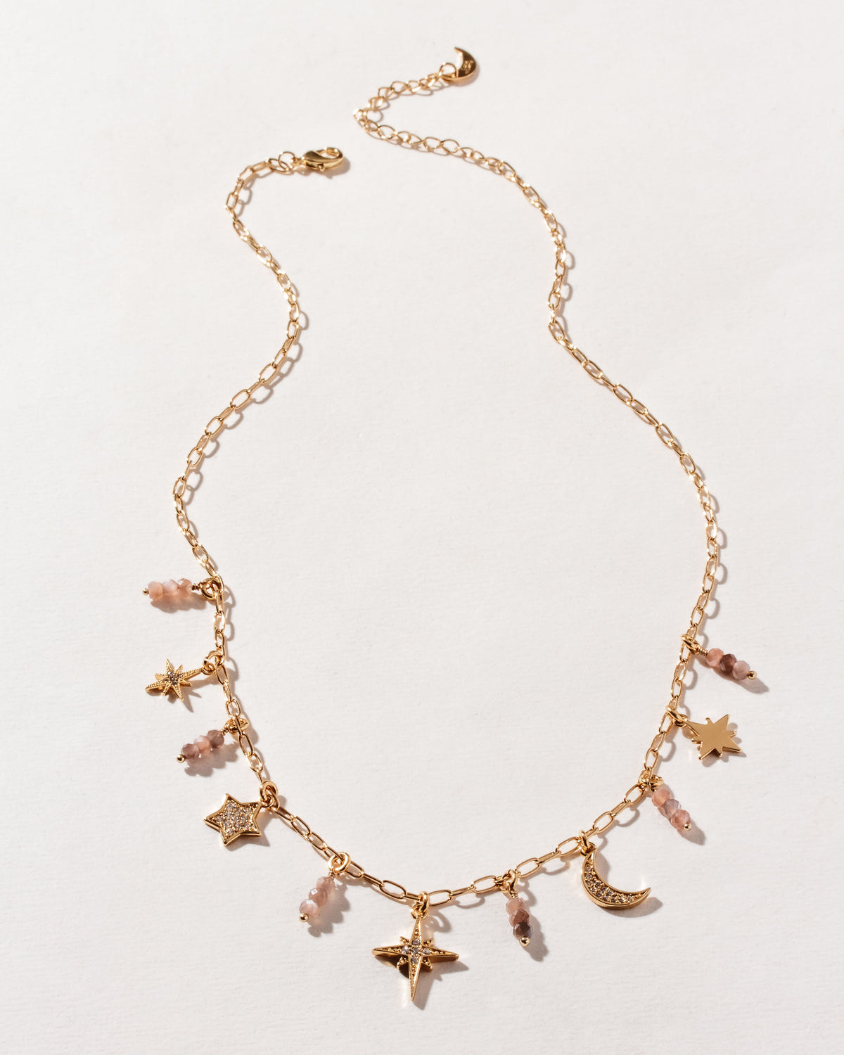 Gold chain necklace with many star, and coffee moonstone beads on a white surface.