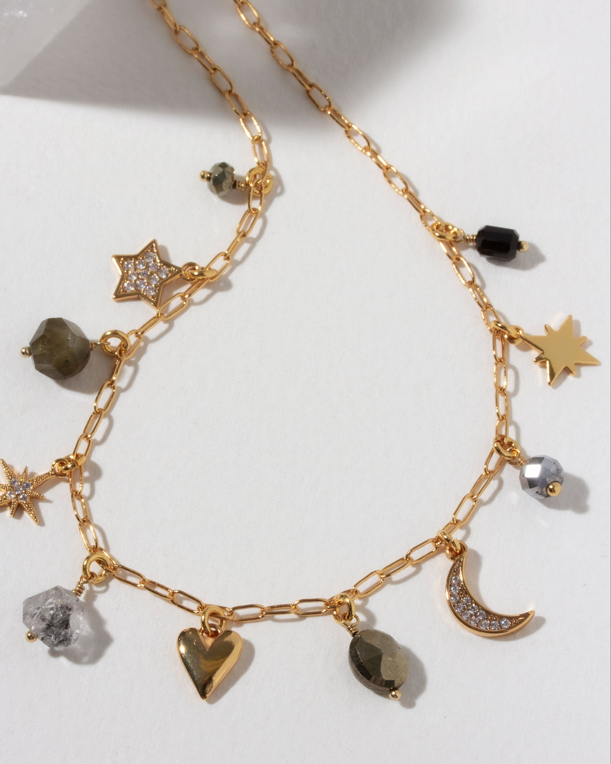 Gold necklace with many celestial gold and cz and gemstone charms on a light background