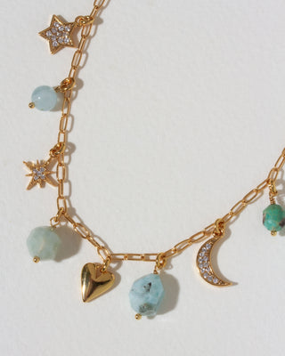 Closeup of gold necklace with many celestial gold and cz and gemstone charms on a light background