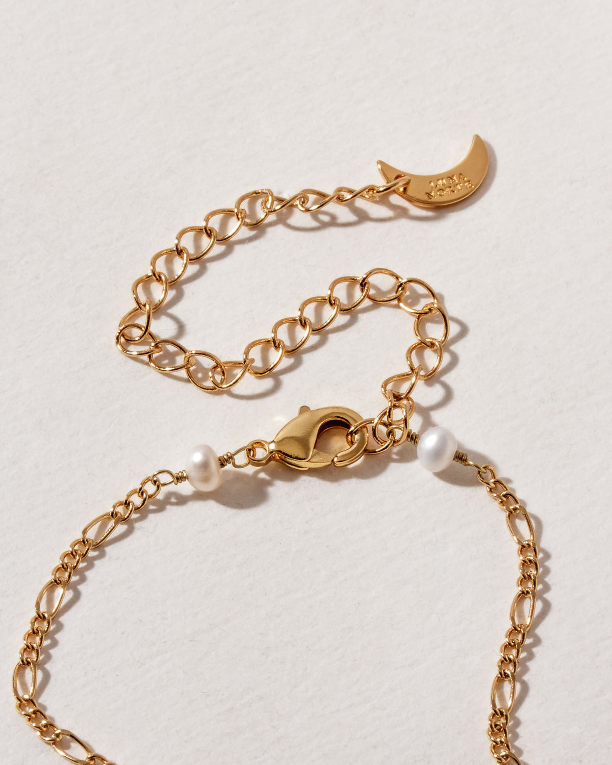 Close up of gold plated necklace showing lobster clasp, extension chain, and pearl beads.
