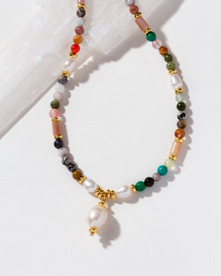 A beaded necklace with white pearls, green and orange stones, pink beads, and gold spacer rings.