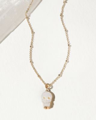 A delicate gold chain necklace featuring a small skull pendant with a white mother of pearl face and gold accents.