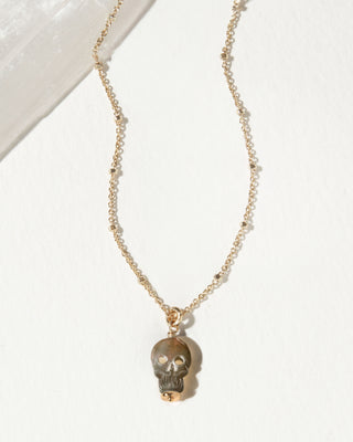 A gold chain necklace featuring a small skull pendant carved from black lip mother of pearl.