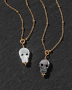 Two gold chain necklaces with skull pendants, one featuring a translucent white skull and the other a translucent gray skull.