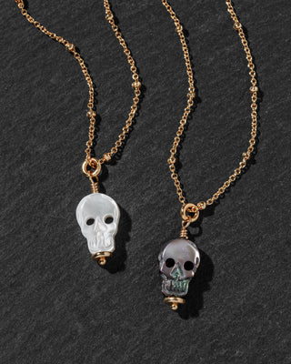 Two gold chain necklaces with skull pendants, one featuring a translucent white skull and the other a translucent gray skull.