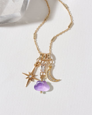A gold-toned chain necklace with a cluster of charms, including a gold Polaris star, a gold crescent moon set with clear CZ's, and a purple amethyst cloud charm.