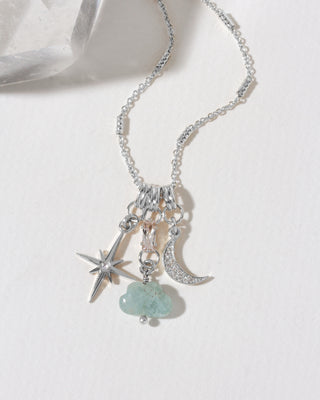 A silver-toned celestial charm necklace featuring a star, crescent moon, and a light blue cloud-shaped pendant.