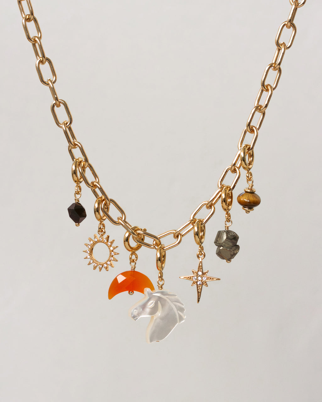Gold necklace with various charms on a light gray background