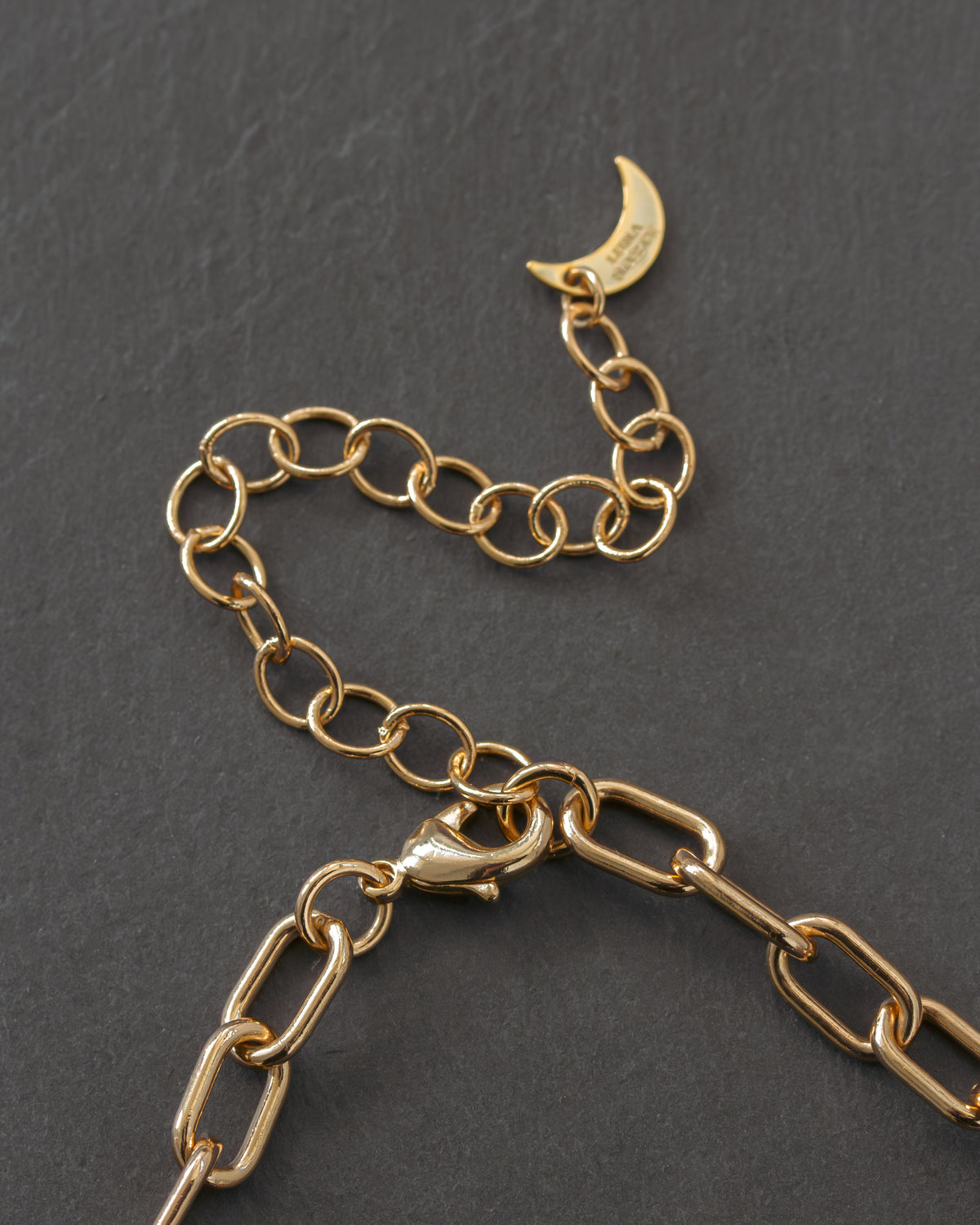 Gold chain necklace extender chain with a crescent moon logo charm on a dark gray background