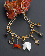 Gold charm necklace with various charms on a dark surface