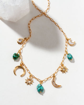 Gold necklace with turquoise beads and moon, star, and sun charms on a white background