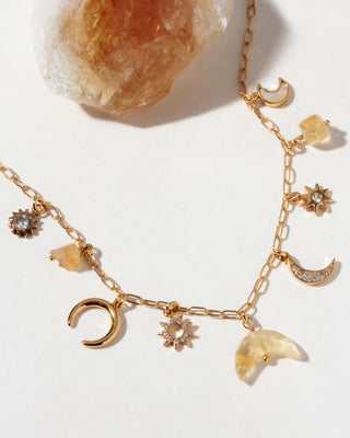 Gold necklace with many celestial gold and cz and citrine gemstone charms on a light background