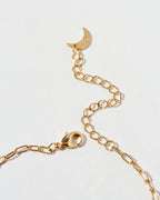 Closeup of gold chain necklace lobster closure with a crescent moon charm on a light gray background