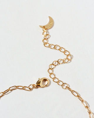Closeup of gold chain necklace lobster closure with a crescent moon charm on a light gray background