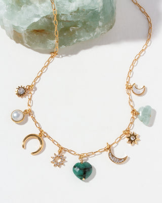 Gold necklace with various CZ, emerald, mother-of-pearl, aquamarine, and pearl charms on a white background.