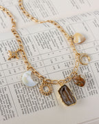 Gold necklace with various gemstone and celestial charms on a printed paper background