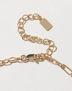 Close-up of the Onyx & Moonlight Charm Necklace's gold clasp and chain extender, with a brand tag.
