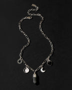 A silver-toned chain necklace with multiple charms, including a sun, a heart, a crescent moon, a moon phase, and a labradorite crystal pendant, displayed on a dark textured background.