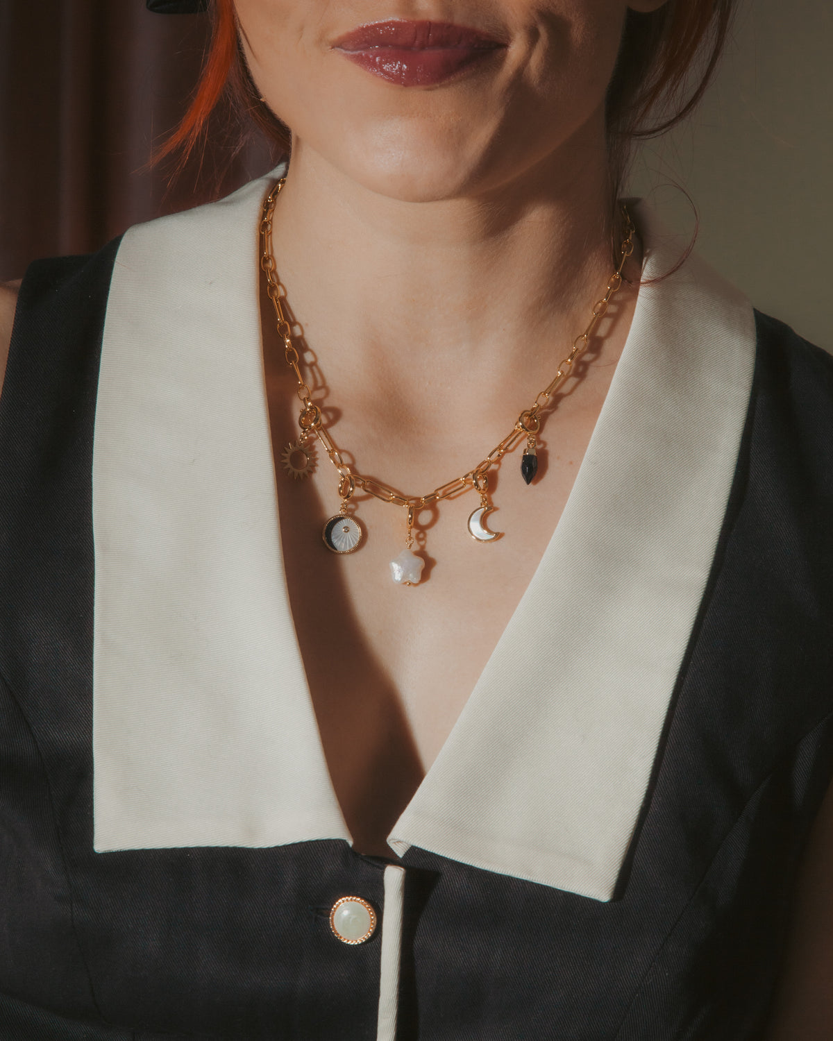 Close-up of a person wearing a gold necklace with various charms against a neutral background