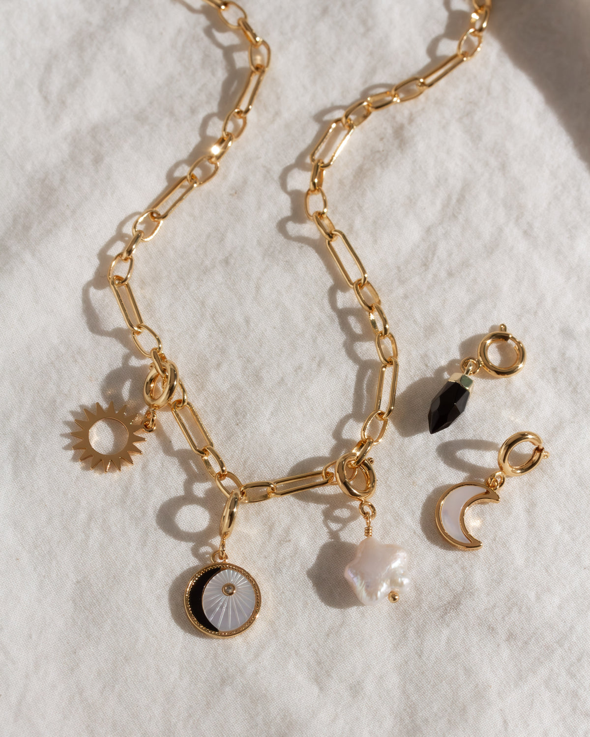 Gold paperclip chain necklace with five charms including pearl, onyx, star, crescent moon, and sun.