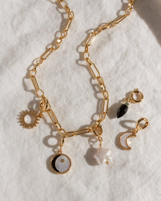 Gold chain necklace with various charms on a white background