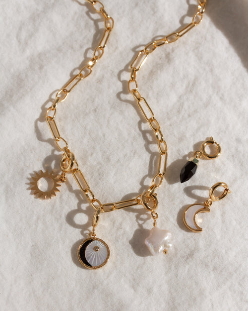 Gold chain necklace with various charms on a white background
