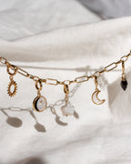 Gold chain necklace with various charms on a white fabric background