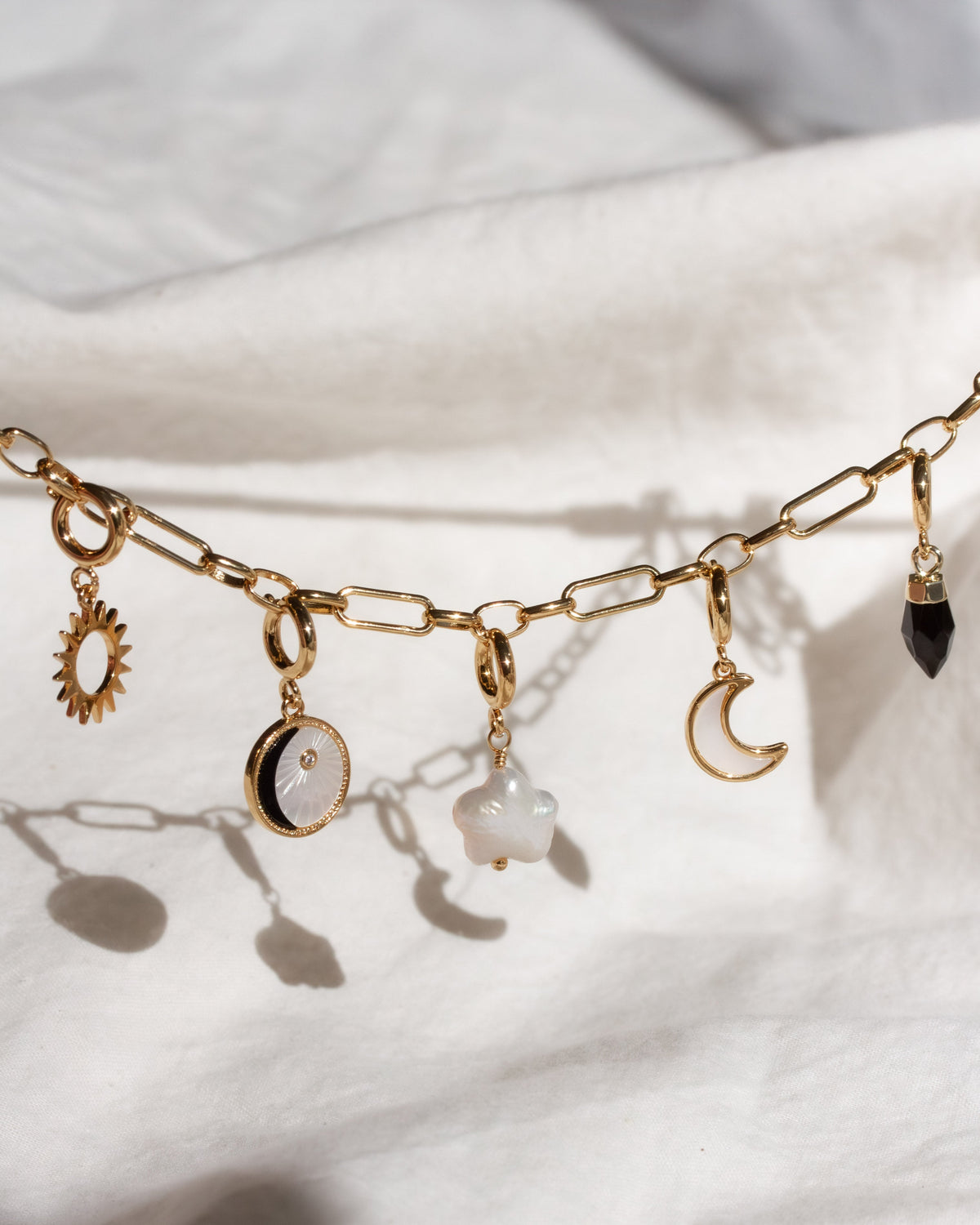 Gold chain necklace with various charms on a white fabric background