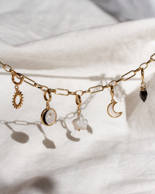 Gold chain necklace with various charms on a white fabric background