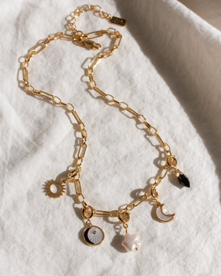 Gold chain necklace with various charms on a white fabric background