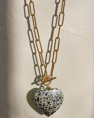 A gold chain toggle front CZ necklace with a speckled white and black dalmatian jasper stone heart-shaped pendant.