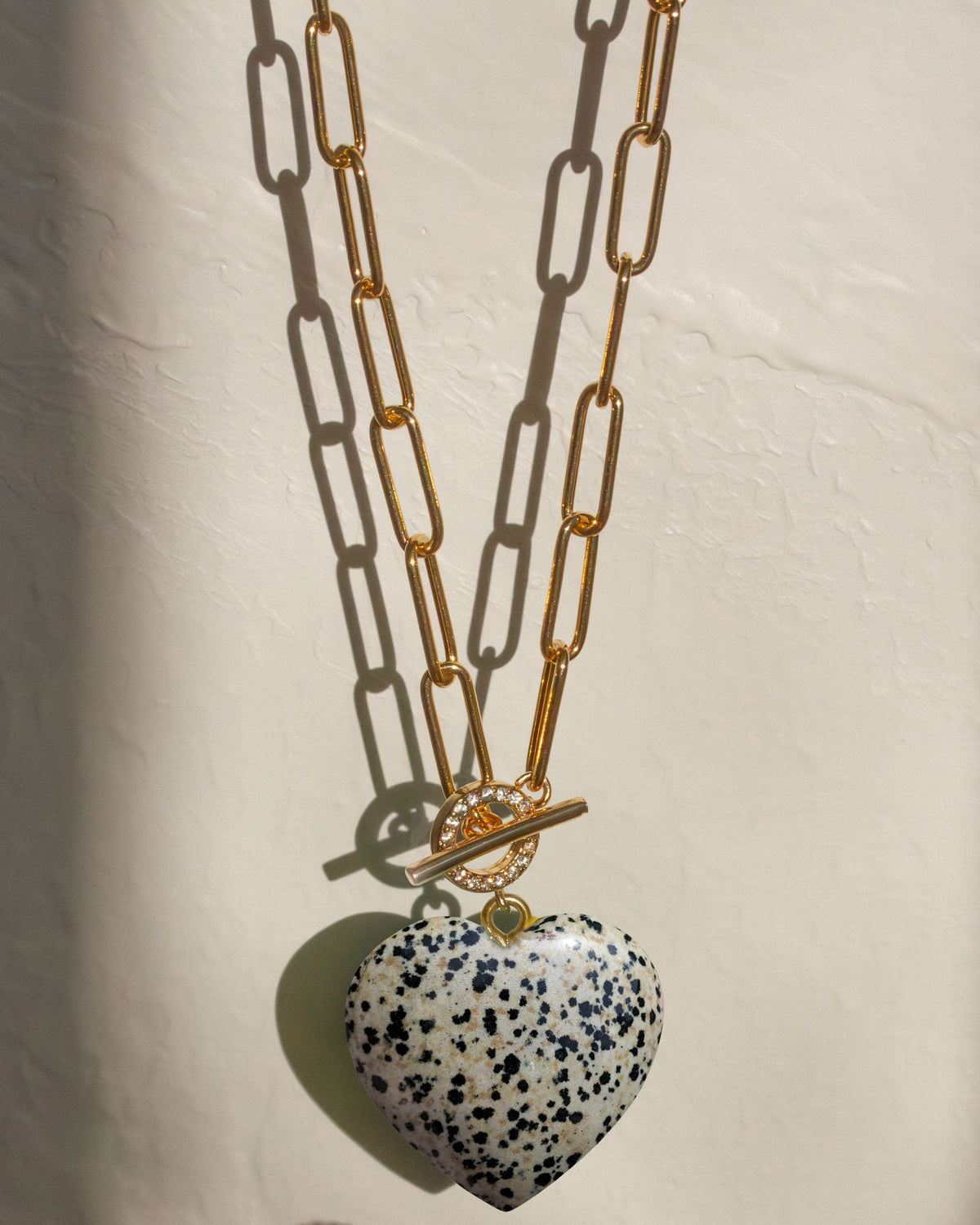 A gold chain toggle front CZ necklace with a speckled white and black dalmatian jasper stone heart-shaped pendant.