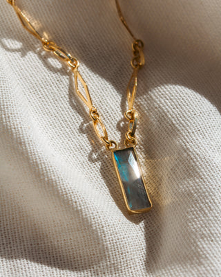 Gold necklace with a blue pendant on a beige fabric background