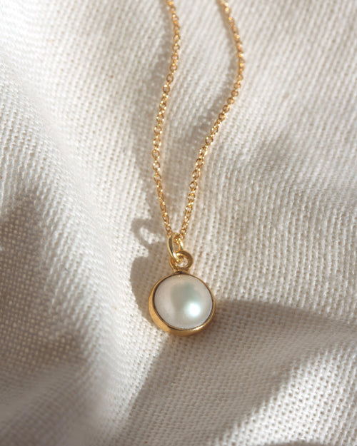 Gold necklace with a round pendant on a textured beige background