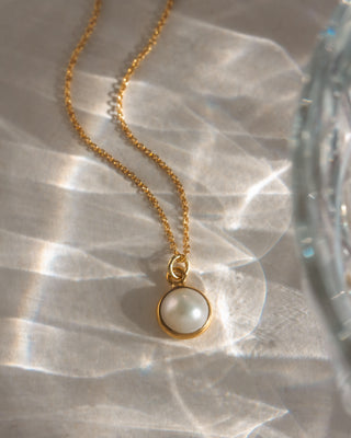 Gold necklace with a pearl pendant on a reflective surface