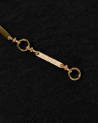A close-up of a gold-toned metal chain link with a rectangular bar engraved with 'Luna Norte' and two circular rings, set against a textured black background.