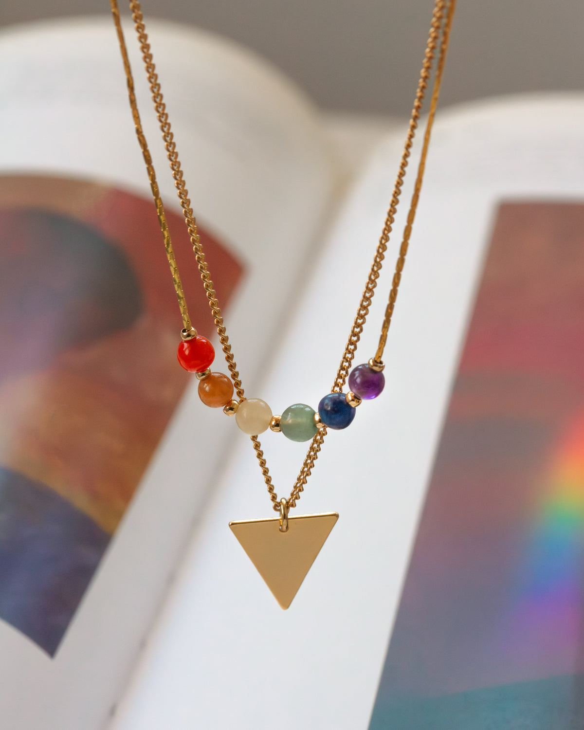 Necklace with colorful beads and a gold triangle pendant on a blurred background
