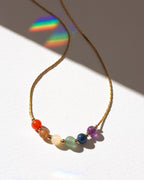 Gold-plated necklace with colorful gemstone beads casting a rainbow shadow