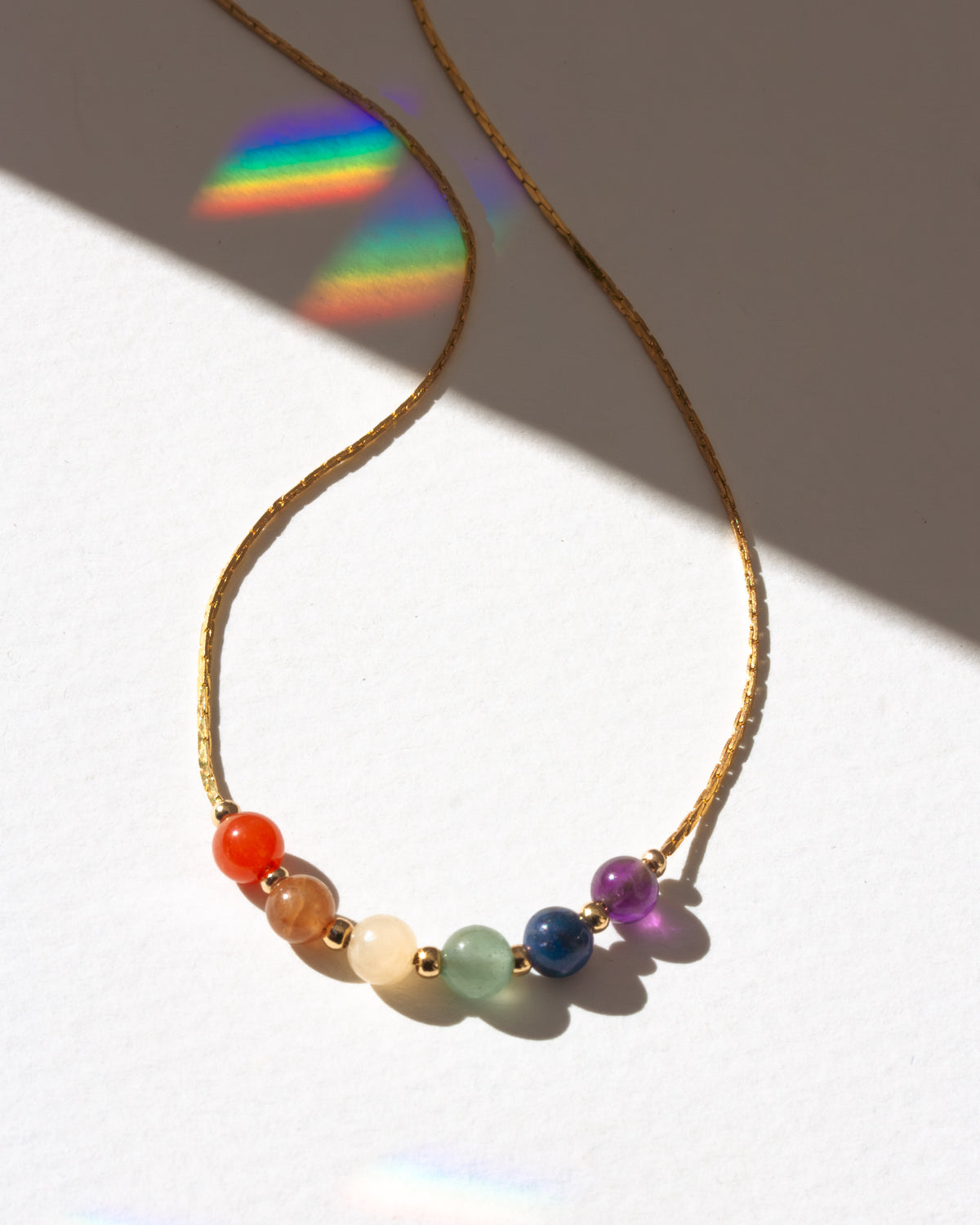 Gold-plated necklace with colorful gemstone beads casting a rainbow shadow