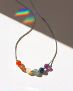 Rhodium necklace with colorful beads casting a rainbow shadow on a white surface