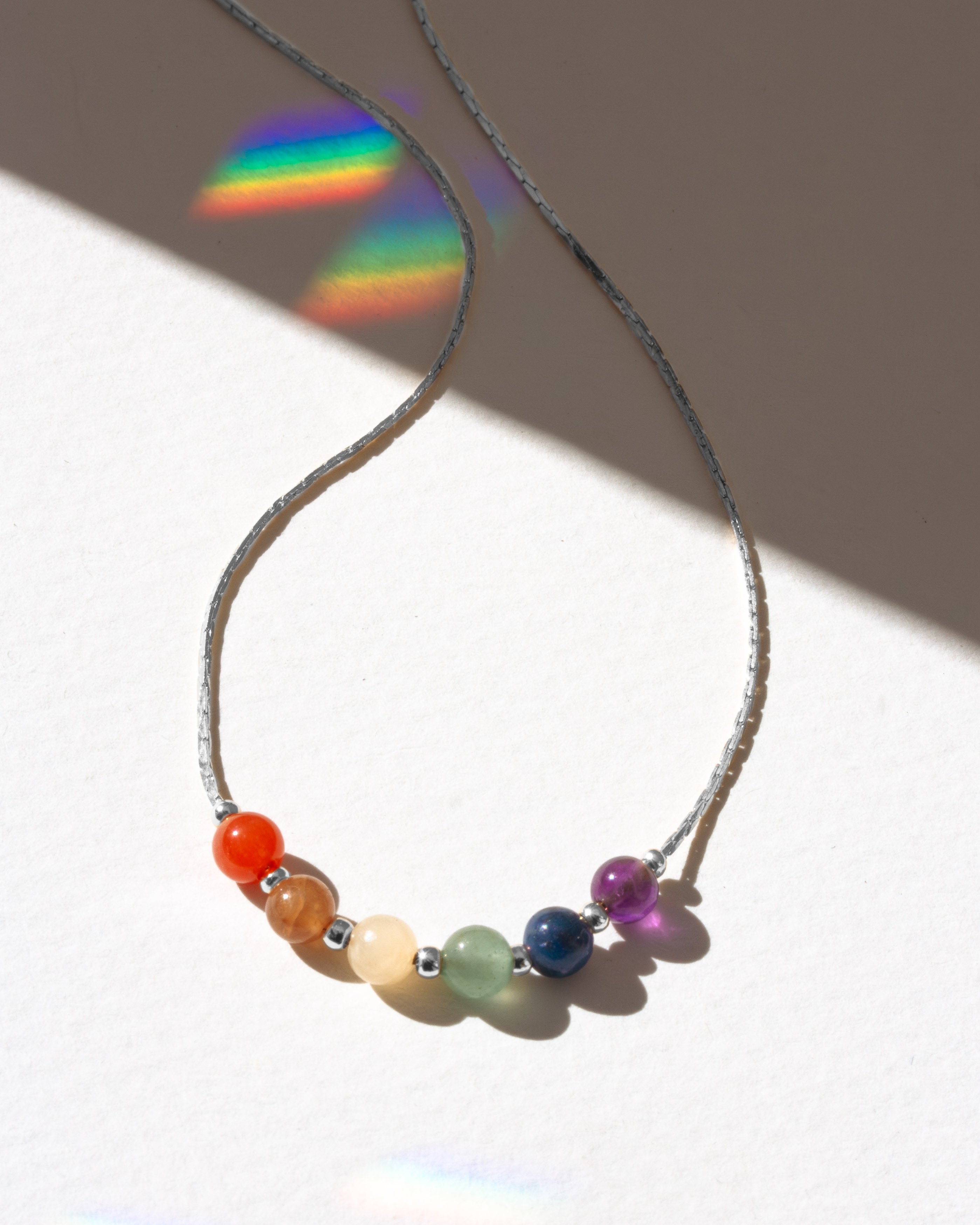 Rhodium necklace with colorful beads casting a rainbow shadow on a white surface