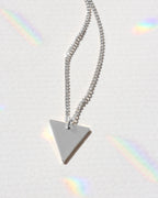Silver triangle pendant necklace on a light gray background with rainbow shadows