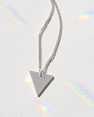 Silver triangle pendant necklace on a light gray background with rainbow shadows