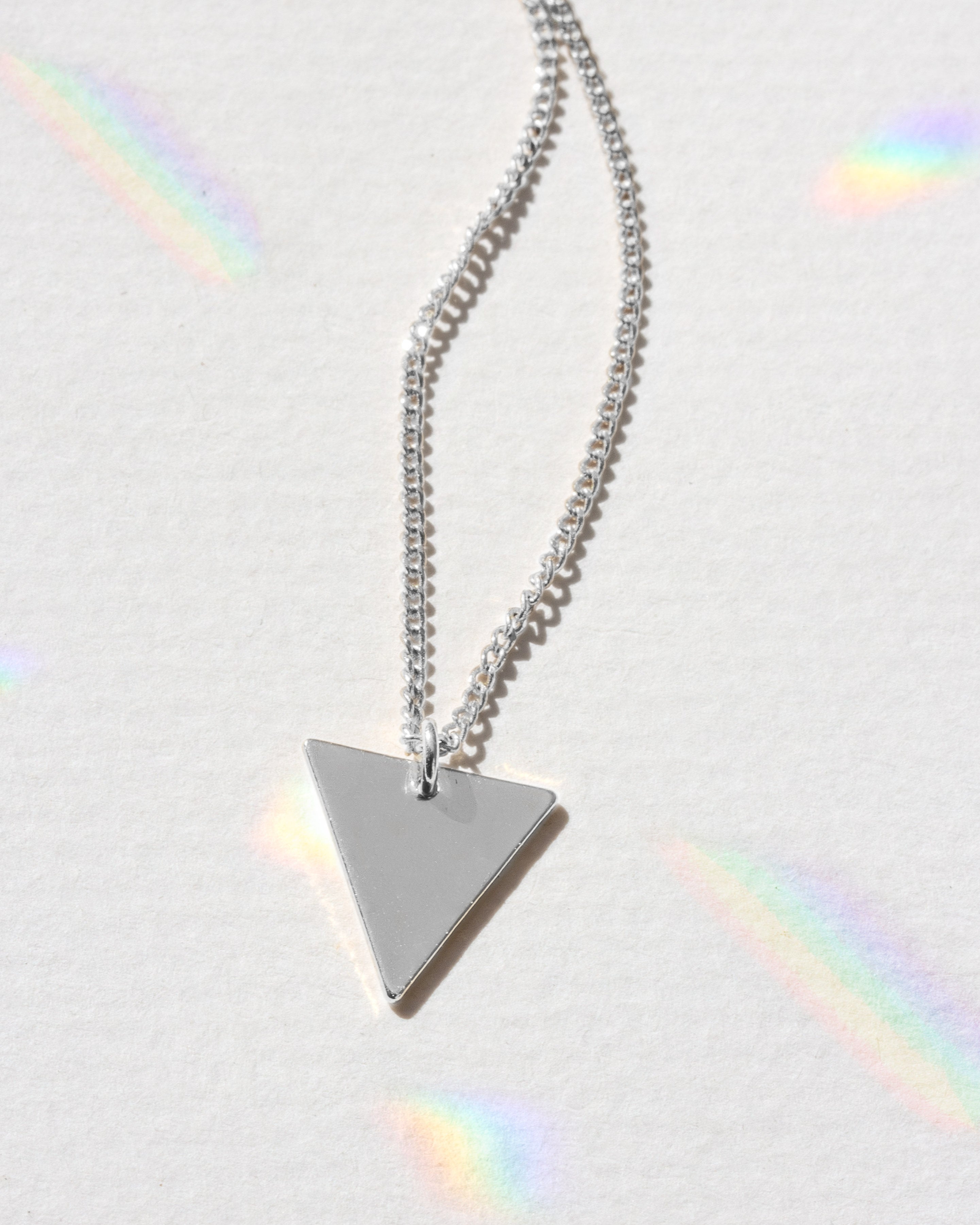 Silver triangle pendant necklace on a light gray background with rainbow shadows