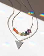 Necklace with colorful beads and a triangle pendant on a reflective surface