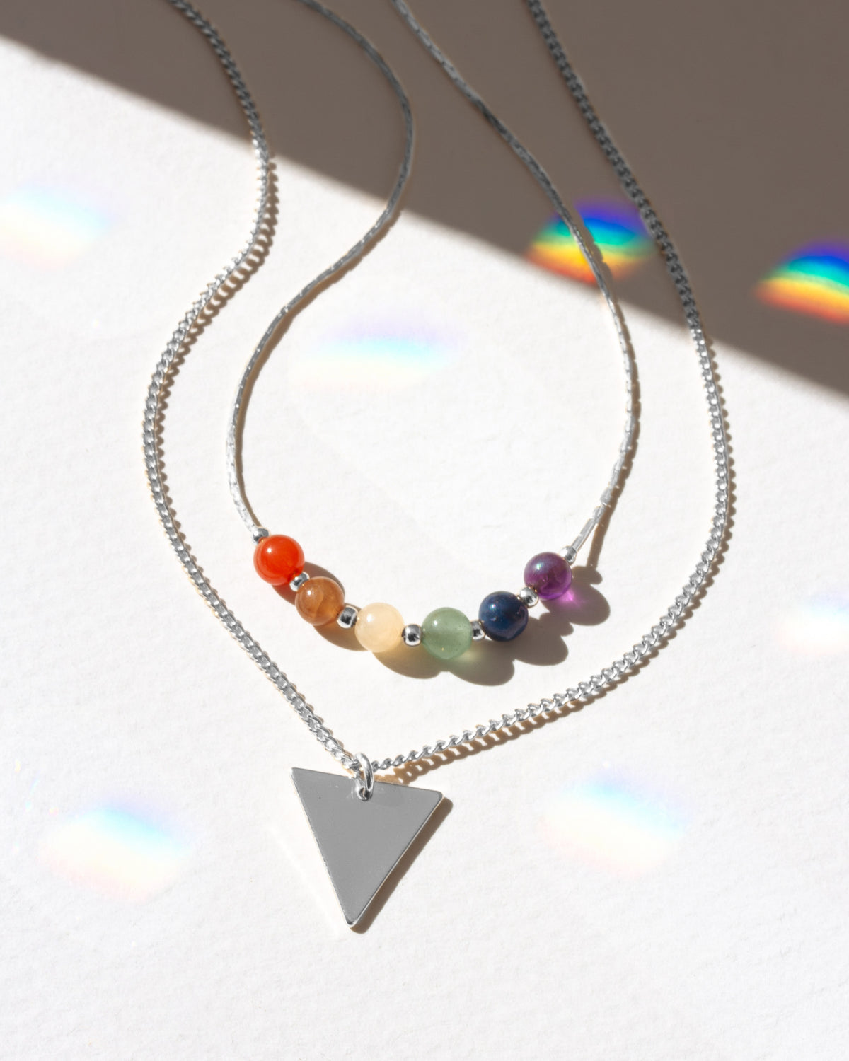 Necklace with colorful beads and a triangle pendant on a reflective surface