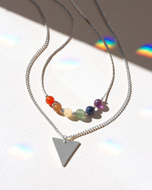 Necklace with colorful beads and a triangle pendant on a reflective surface